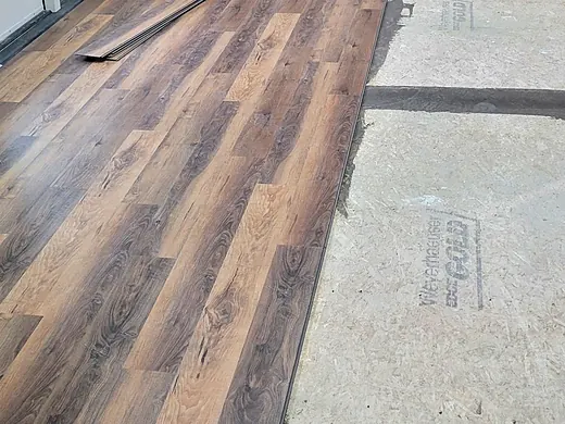 Plank flooring installation in progress beside a stone fireplace