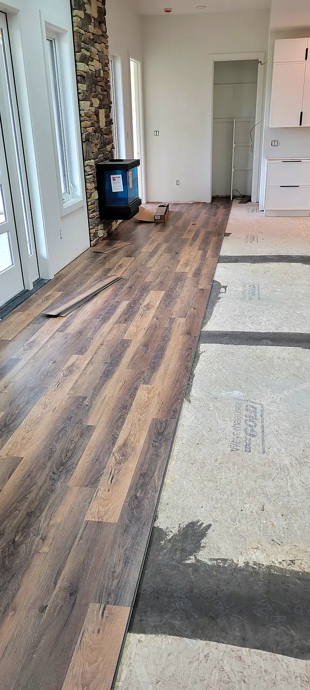 Plank flooring installation in progress beside a stone fireplace
